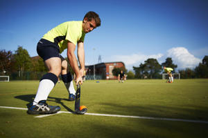 man in a yellow top about to strike a hockey ball onto the pitch