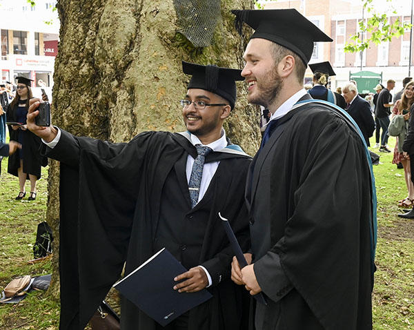 Two male students are taking photos of themselves during graduation