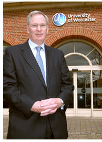 The Duke of Gloucester is wearing a suit and standing outside the main entrance to the University