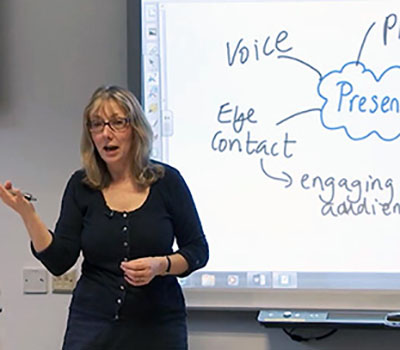 A woman is standing next to a whiteboard talking